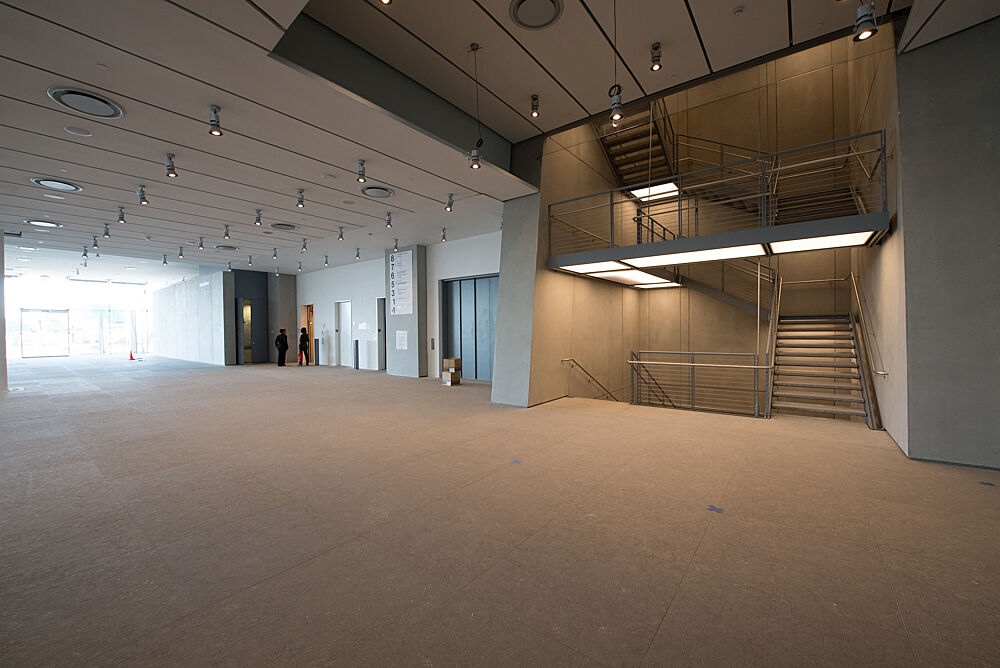 The Griffin Hall Gallery, empty, in daylight at the Whitney Museum of American Art. The image shows the room designed by Renzo Piano, with windows far to the left and a staircase toward the right. 